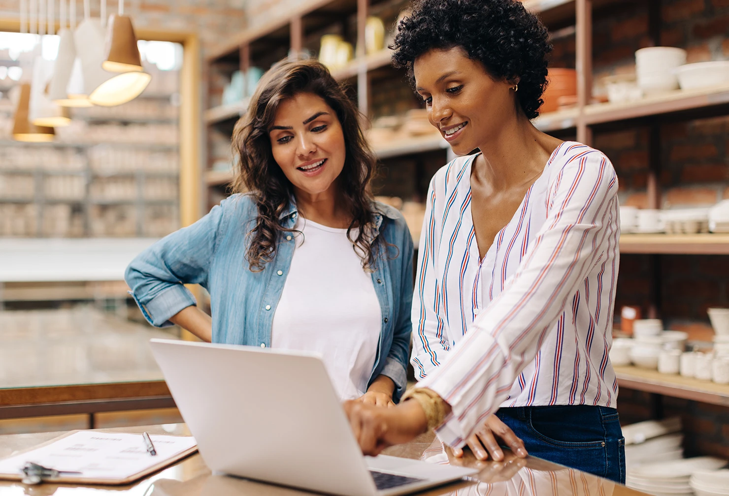 A pair of female small business owners in discussion, while standing around a laptop 