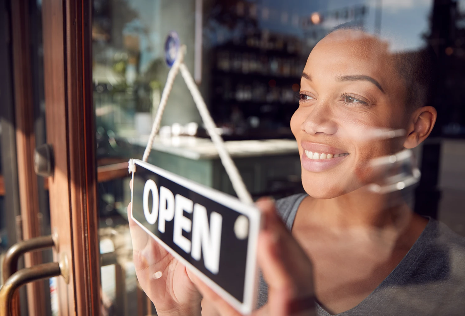 A female small business owner smiling while changing the open/closed sign in the glass doorway